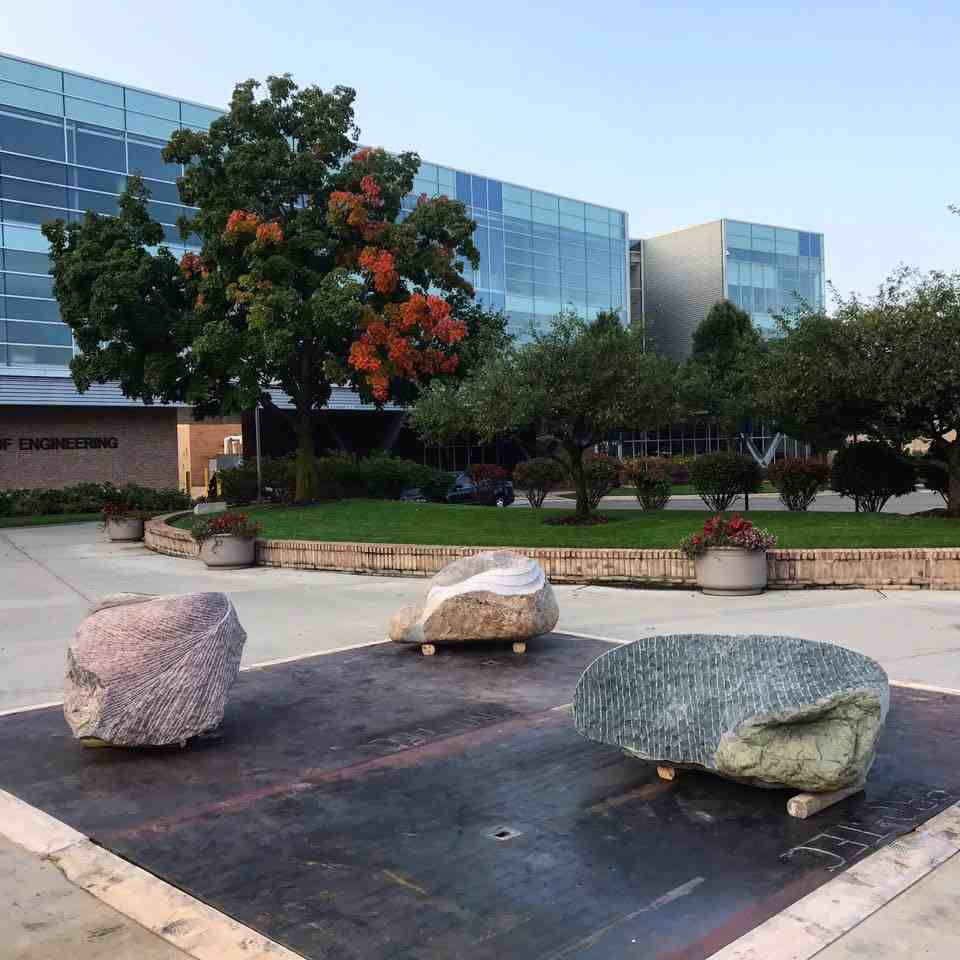 Outdoor sculpture of three carved stones on a metal platform.